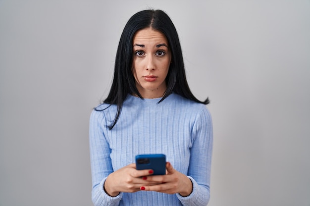 Hispanic woman using smartphone skeptic and nervous, frowning upset because of problem. negative person.