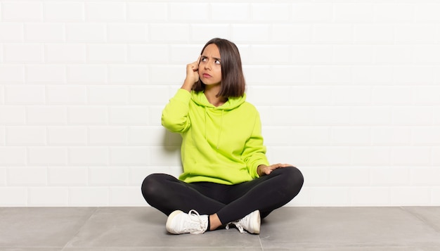 Hispanic woman with a concentrated look, wondering with a doubtful expression, looking up and to the side