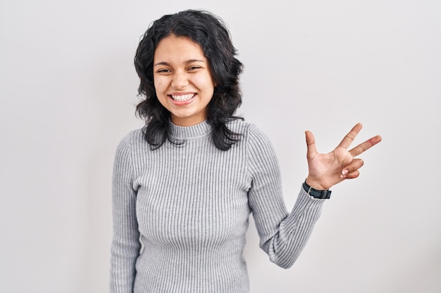 Hispanic woman with dark hair standing over isolated background showing and pointing up with fingers number three while smiling confident and happy.