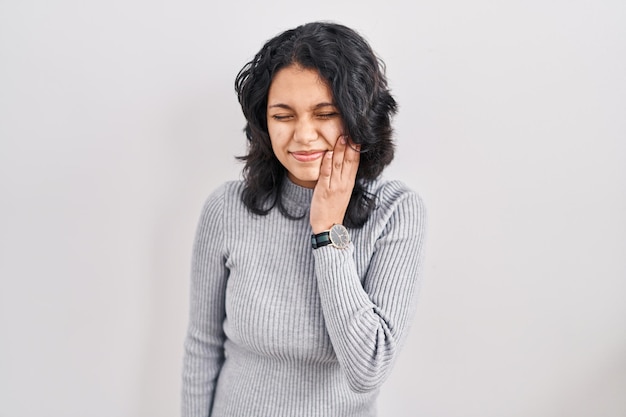 Hispanic woman with dark hair standing over isolated background touching mouth with hand with painful expression because of toothache or dental illness on teeth dentist