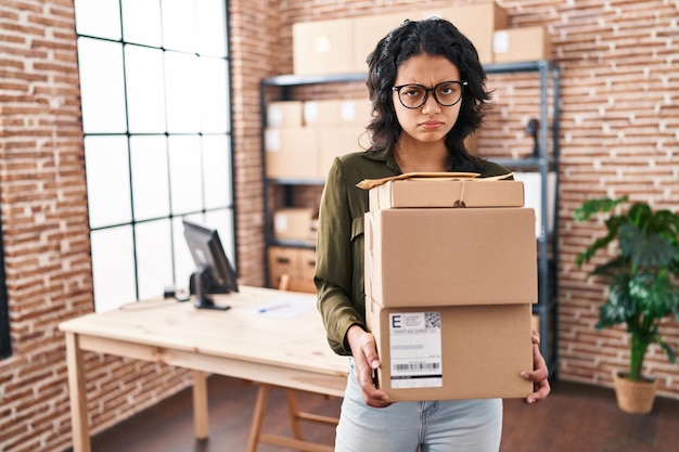 Hispanic woman with dark hair working at small business ecommerce holding boxes depressed and worry for distress, crying angry and afraid. sad expression.