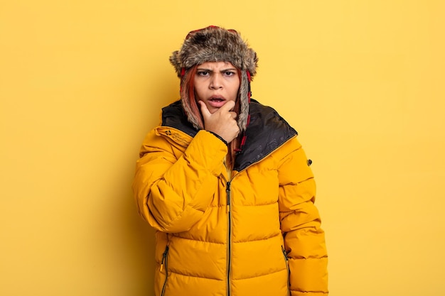 Hispanic woman with mouth and eyes wide open and hand on chin. winter concept