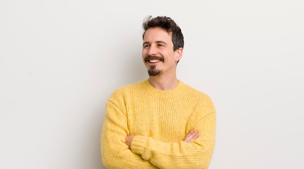 Hispanic young man feeling happy proud and hopeful wondering or thinking looking up to copy space with crossed arms