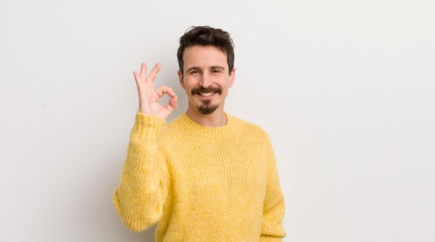 Испаноязычный молодой человек чувствует себя счастливым, расслабленным и довольным, показывая одобрение с хорошо улыбающимся жестом