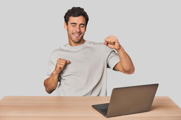 Hispanic young man working on laptop dancing and having fun