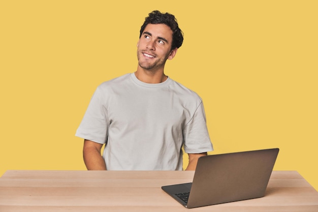 Hispanic young man working on laptop relaxed and happy laughing neck stretched showing teeth