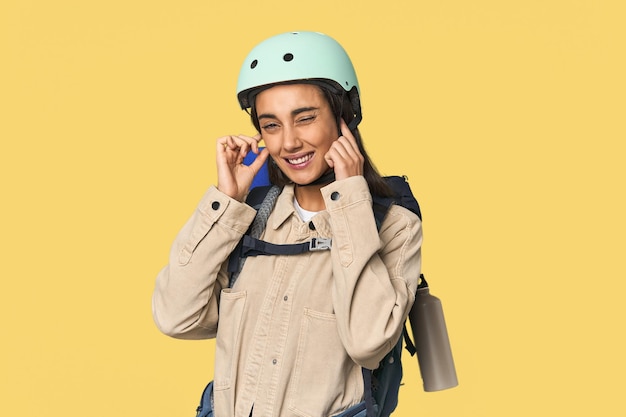 Hispanic young woman with mountain gear covering ears with hands