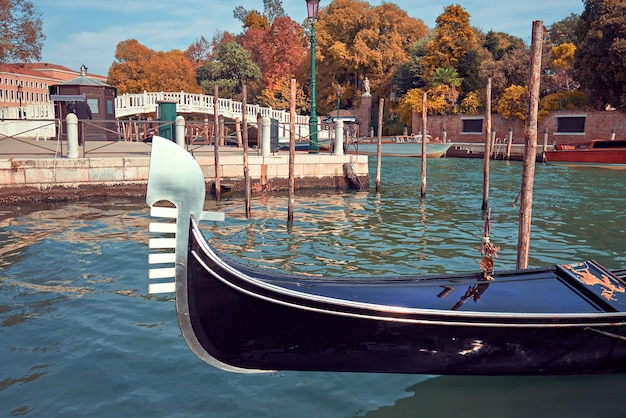 Историческая гондольная лодка в Венеции, Италия, на Гранд-канале недалеко от Плаццале-Рома осенью, с золотыми и желтыми деревьями и историческим мостом позади. Осень в Венеции.