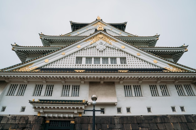 исторический замок в осаке, стоящий на фоне ясного неба. мирный зелено-белый дворец, где никого нет в японии. старое японское традиционное здание с множеством окон, кирпичной крышей и каменной стеной.