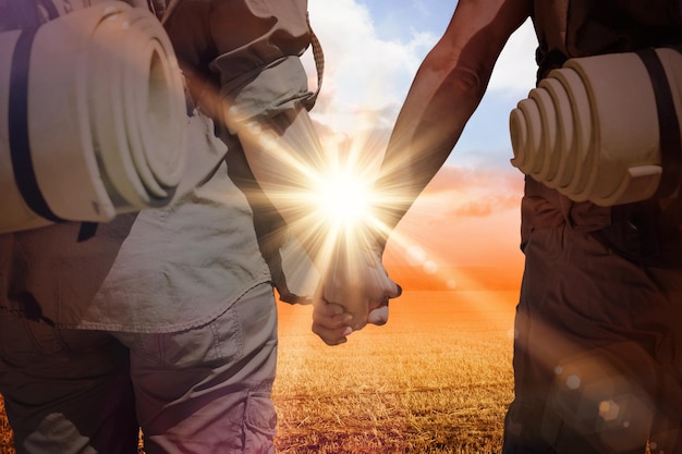 Hitch hiking couple standing holding hands on the road against sunrise over field