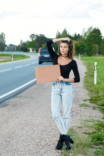 Hitchhiker on the road is holding a blank cardboard sign