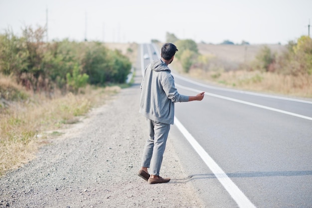 Hitchhiking indian man travelling by hitchhike on road side on highway