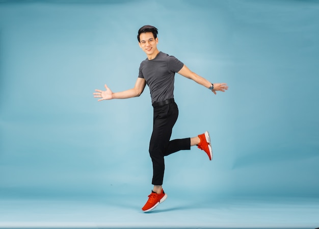 Hnadsome Asian man jumping isolated over blue wall.