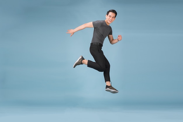Hnadsome Aziatische man veel plezier met springen geïsoleerd over blauwe muur achtergrond