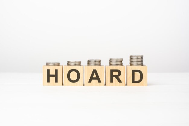 HOARD text written on wooden block with stacked coins on white background