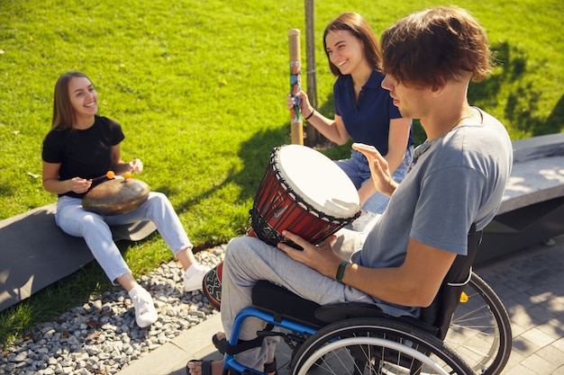 Hobby. Gelukkige gehandicapte man in een rolstoel die tijd doorbrengt met vrienden die buiten live instrumentale muziek spelen. Concept van sociaal leven, vriendschap, mogelijkheden, inclusie, diversiteit.