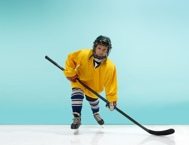 A hockey player in uniform with equipment over a blue studio background. The athlete, child, sport, action concept