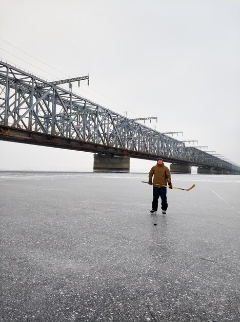 Hockey player on the Volga River with a stick against the backdrop of a large bridge in Ulyanovsk