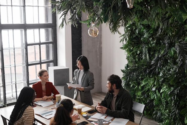 Hoge hoek portret van diverse groep zakenmensen die bijeenkomen aan tafel in een modern kantoorinterieur versierd met planten, kopieer ruimte