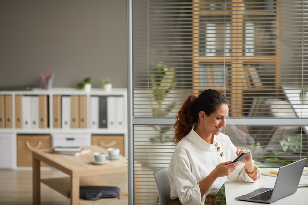 Hoge hoek portret van elegante succesvolle zakenvrouw met behulp van smartphone en glimlachen terwijl u geniet van werk vanuit huis, kopieer ruimte