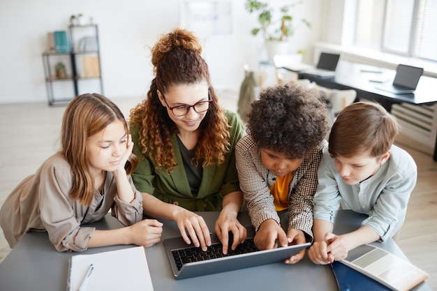 Foto hoge hoek portret van jonge vrouwelijke leraar met behulp van computer met diverse groep kinderen