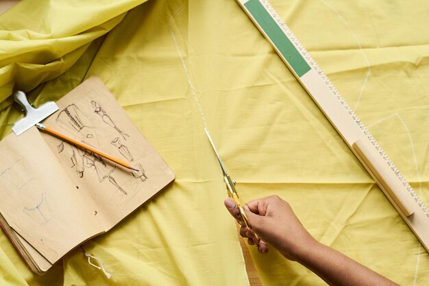 Hoge hoek van de hand van een kleermaker die een schaar vasthoudt tijdens het snijden van textiel op tafel