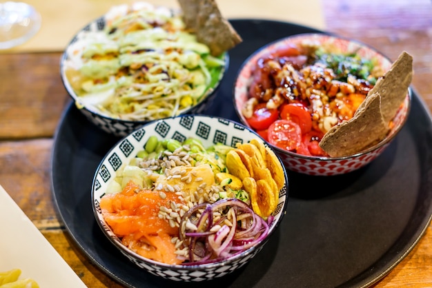 Hoge hoek van heerlijke poke bowls met verschillende groenten en bonen met zaden en ui met vis geplaatst op dienblad op houten tafel in licht restaurant