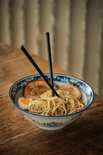 Hoge hoek van heerlijke vers gekookte ramen met noedels, kip en ei in keramische kom geplaatst op houten tafel met stokjes