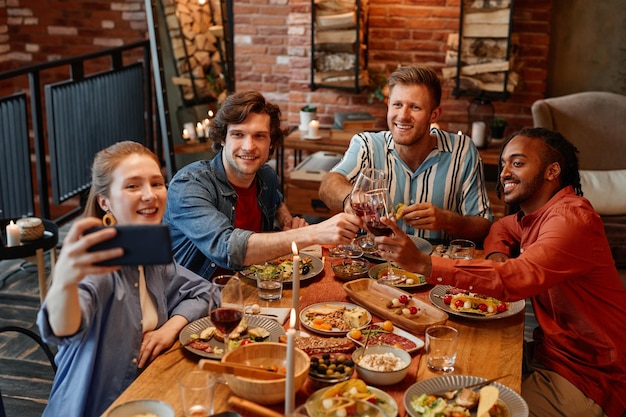 Hoge hoekmening bij een groep vrienden die selfie foto's nemen aan tafel tijdens het etentje en rammelende gl