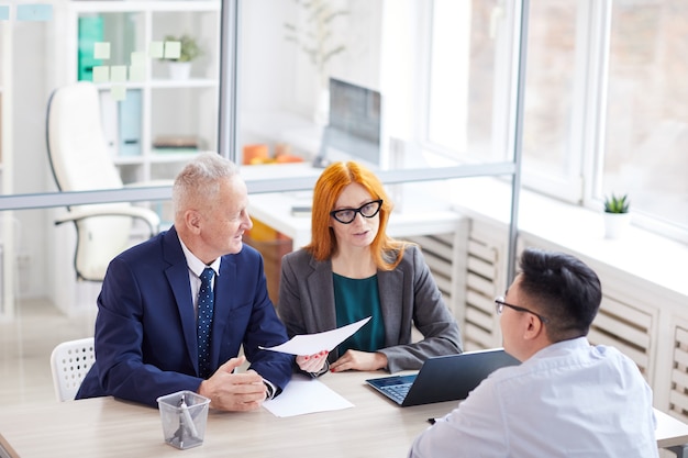 Hoge hoekmening op twee managers interviewen jonge man voor baan op kantoor, kopieer ruimte