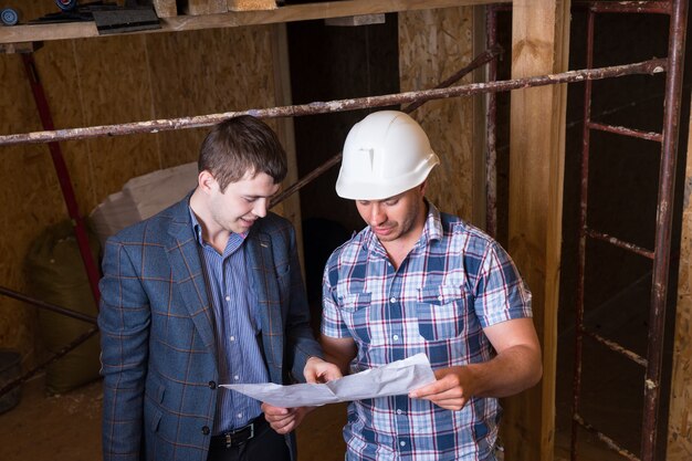 Hoge hoekmening van architect en bouwvakker Foreman inspecteren plannen samen in onvoltooide gebouw