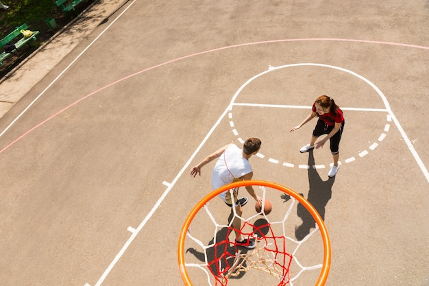 Hoge hoekmening van bord van jonge atletische paar basketbal spelen op buitenbaan op zonnige dag