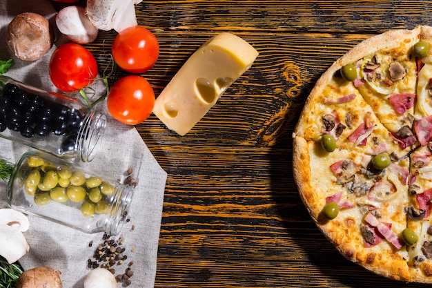 Hoge hoekmening van de helft van de pizza met ham, ui, olijven, in de buurt van leugentomaten, kaas, champignons en andere groenten op servet op houten tafel