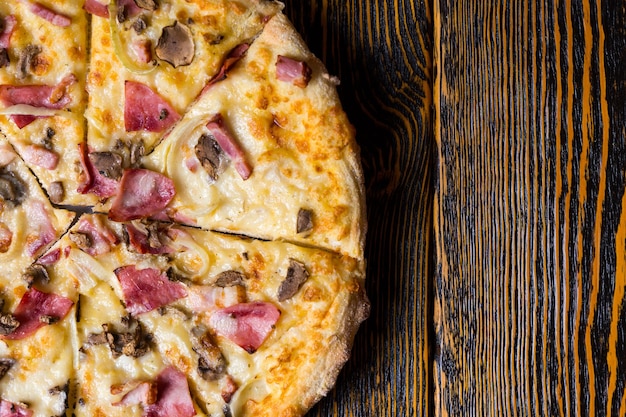 Hoge hoekmening van de helft van heerlijke pizza met ham, champignons en ui op houten tafel