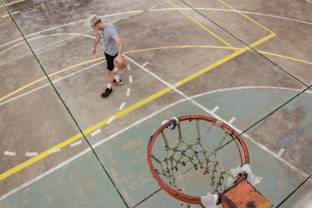 Hoge hoekmening van een jonge man die een basketbal stuitert op een verlaten veld.