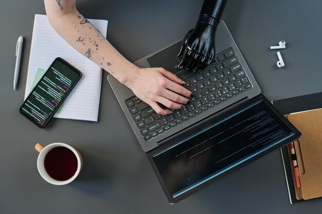 Hoge hoekmening van meisje met prothetische arm typen op laptop aan tafel om online werk te doen