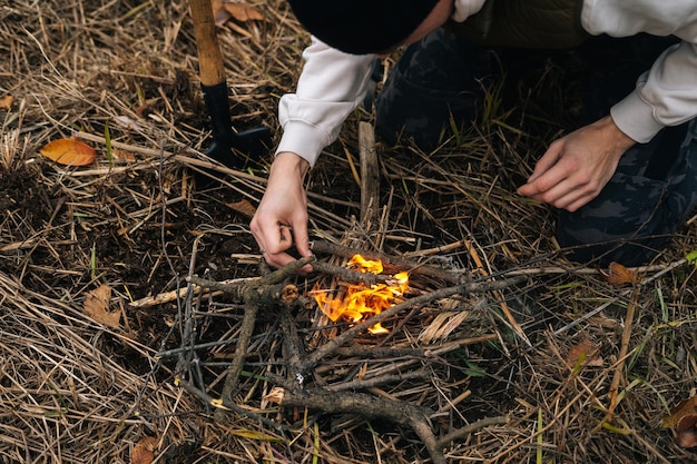 Hoge hoekmening van onherkenbaar overlevingsmannetje dat aanmaakhout op brandend vuur zet om warm te blijven en eten buitenshuis te koken op een bewolkte koude dag