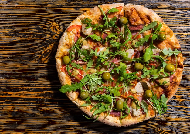 Hoge hoekmening van pizza met rucola-olijven, verschillende toppings en kaas op houten tafel