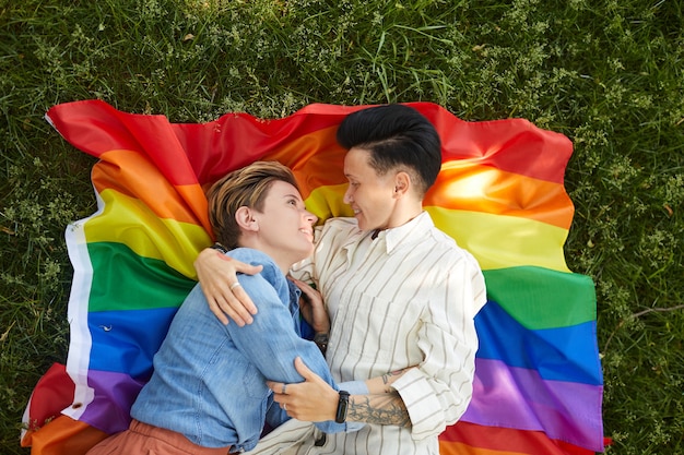 Hoge hoekmening van twee lesbiennes die op gekleurde vlag liggen en tijdens picknick in het park omhelzen