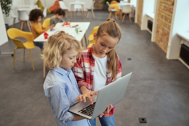 Hoge hoekmening van twee lieve kinderen, kleine jongen en meisje die leren laptop vast te houden en in een