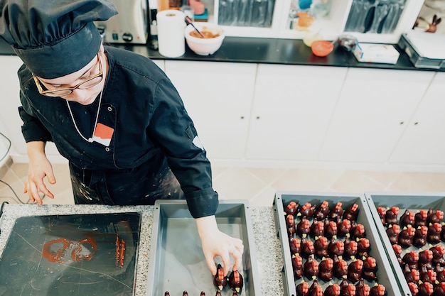 Hoge hoekmening van vrouwelijke chocolatier in uniform van de chef-kok die aan gebak in de keuken werkt