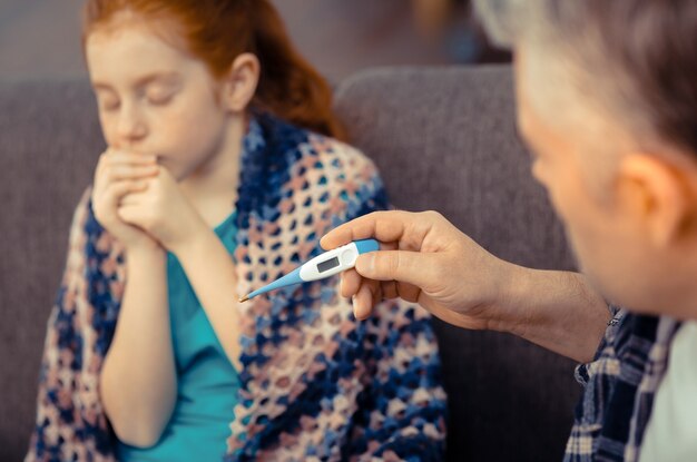 Hoge lichaamstemperatuur. Bovenaanzicht van een professionele elektronische thermometer die de temperatuur van een aardig jong meisje toont