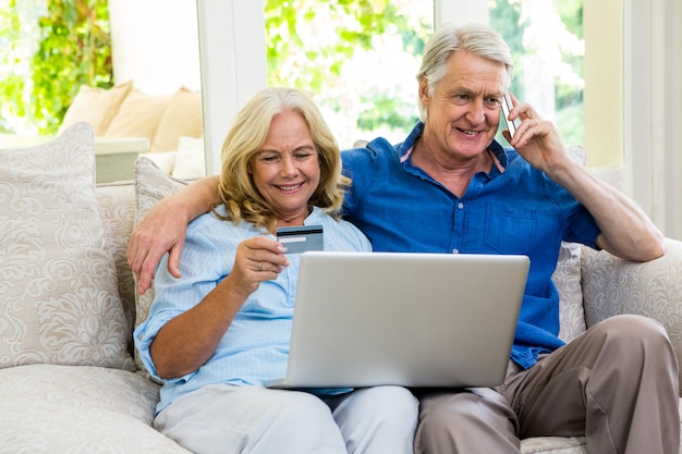 Hoger paar die laptop met behulp van terwijl thuis het spreken op telefoon