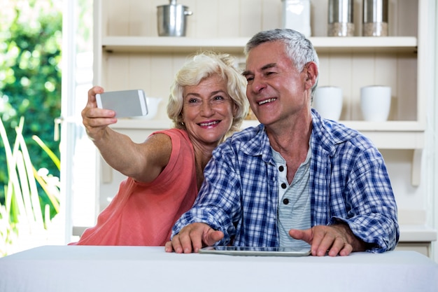 Hoger paar die selfie door mobiele telefoon nemen terwijl het zitten in keuken