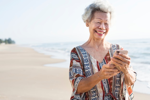 Hogere Aziatische vrouw die een telefoon met behulp van bij het strand