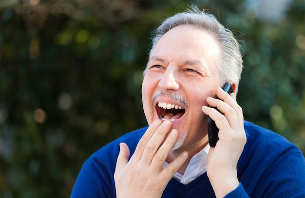 Hogere knappe mens die op de telefoon in een park spreekt