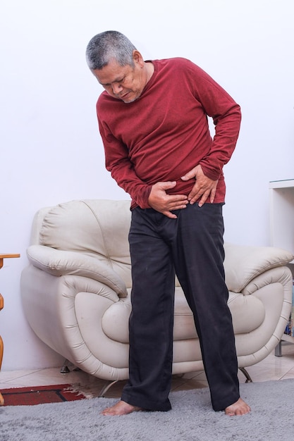 Hogere mannen die zijn maag vasthouden voelen pijn Senior Aziatische man met buikpijn