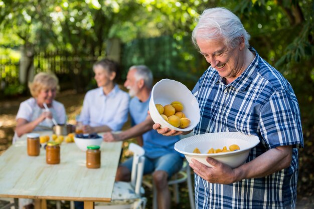 Hogere mens die een kom abrikoos in tuin houdt