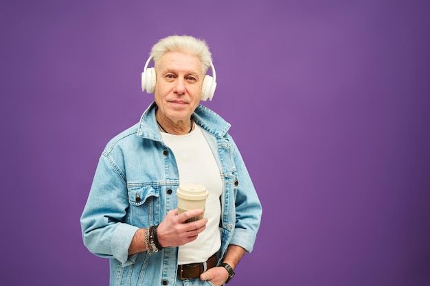 Hogere mens die met wit haar camera bekijkt terwijl het houden van kop van koffie