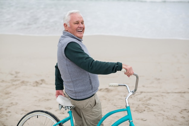 Hogere mens die zich met fiets op het strand bevindt